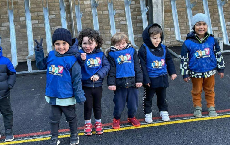 Five Tiny Feet Sports pupils stand joyfully in line while waiting their time to play
